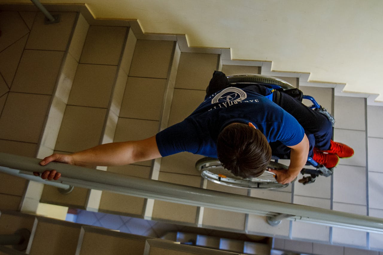 Overhead view of a person in a wheelchair going down stairs indoors, holding onto railings.