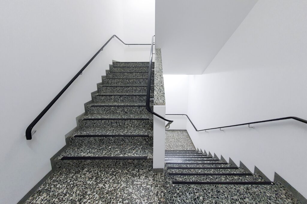 pexels photo 11660580 11660580 Minimalist interior view of a granite staircase with black handrails, featuring clean white walls.