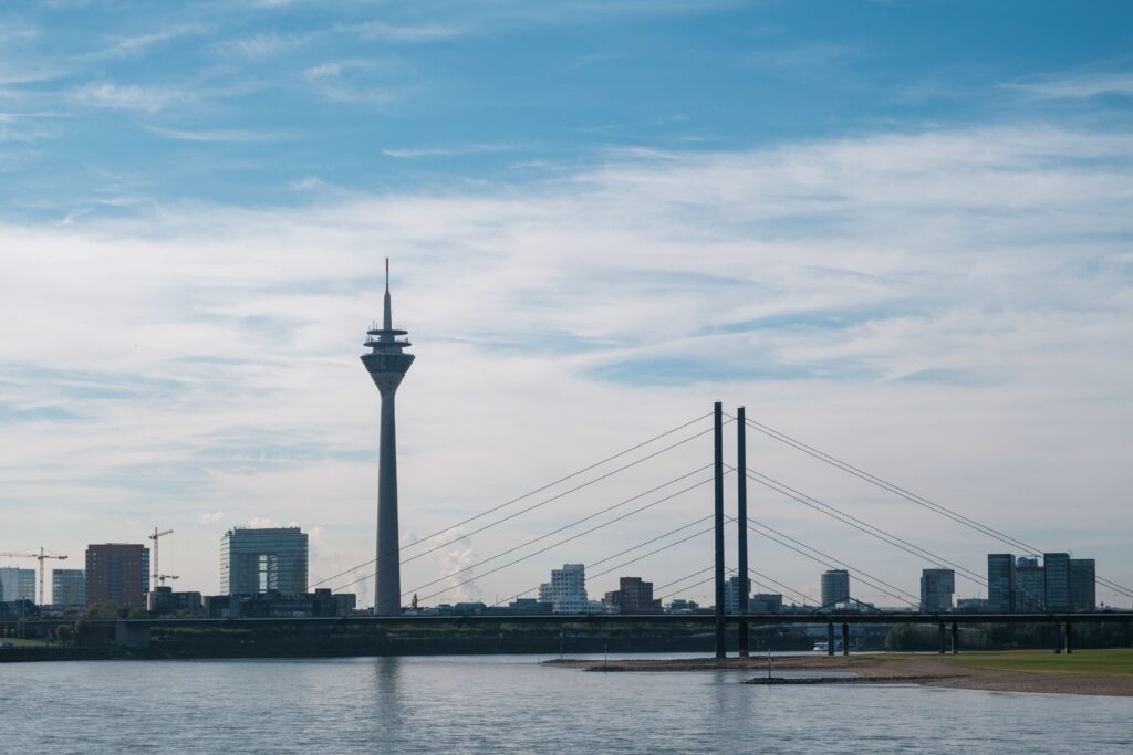 pexels photo 15304077 15304077 Skyline view of Düsseldorf with Rheinturm and bridge spanning the Rhine under a clear blue sky.