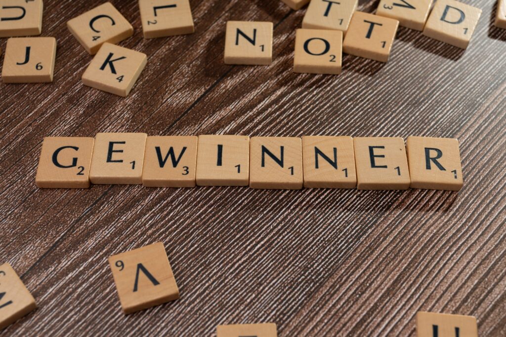 pexels photo 20021294 20021294 Scrabble tiles forming the word 'Gewinner' meaning winner on a wooden table.