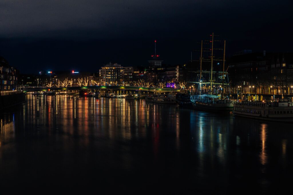 Night view of illuminated Bremen harbor with reflections on the water and city lights.