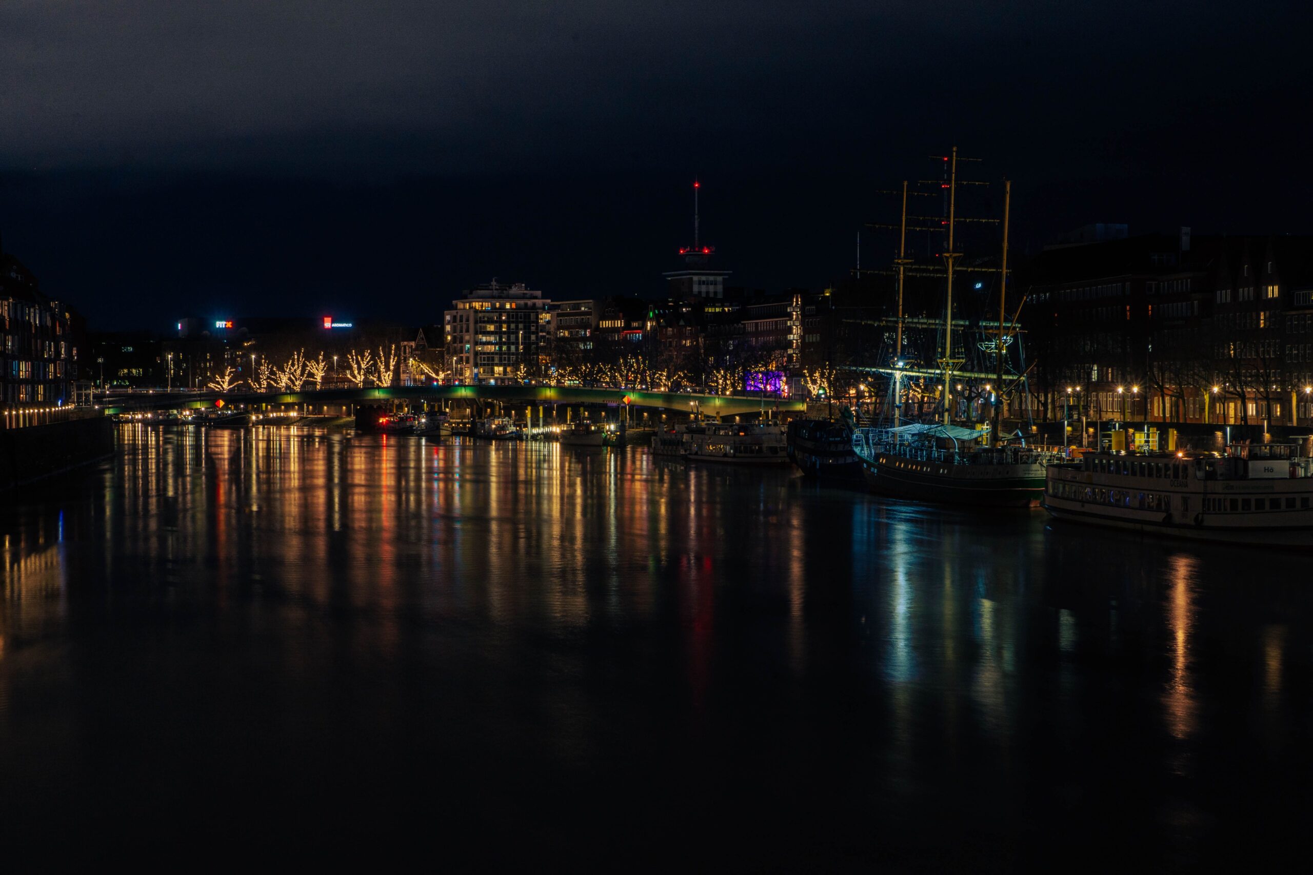 Night view of illuminated Bremen harbor with reflections on the water and city lights.