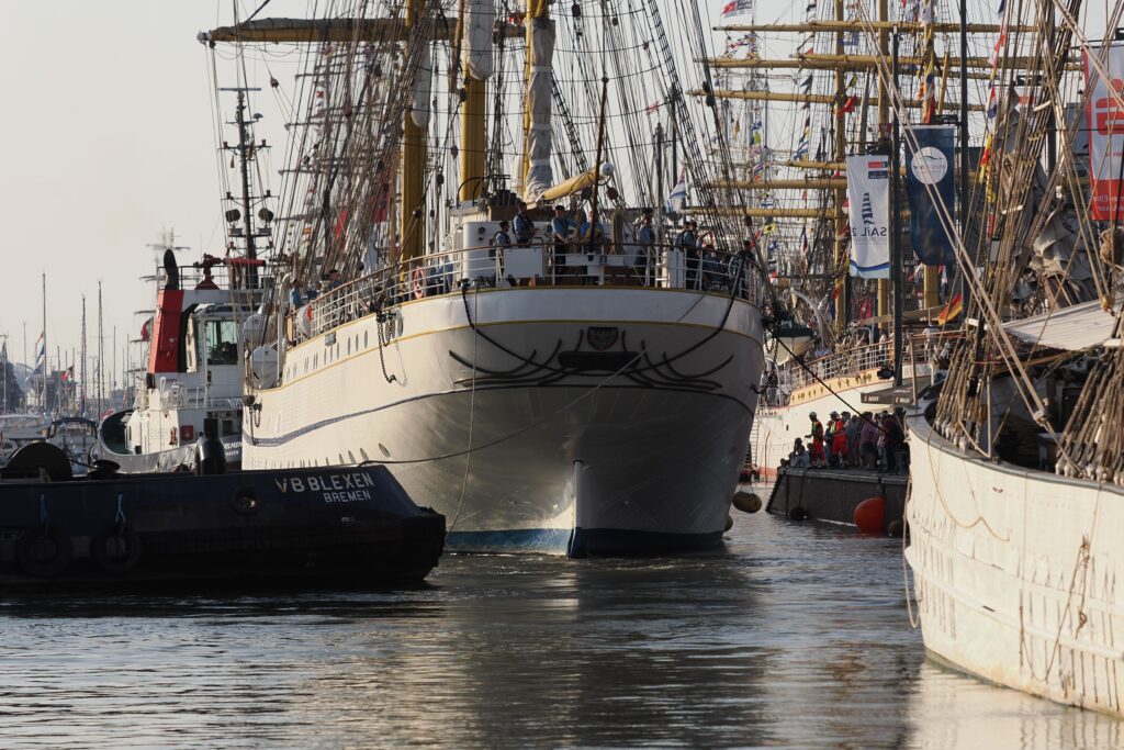 pexels photo 33443761 33443761 A majestic tall ship navigates through Bremerhaven harbor during a maritime festival, crowded with people and colorful flags.