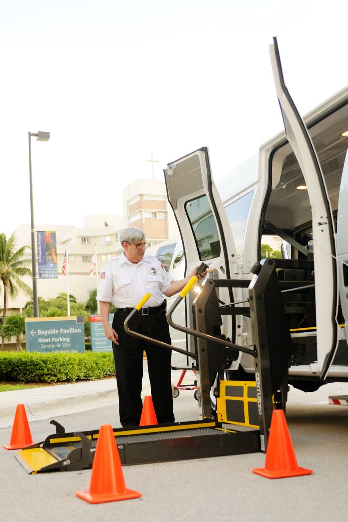 services-04 Safety officer demonstrating the use of a wheelchair lift in a van at a facility.