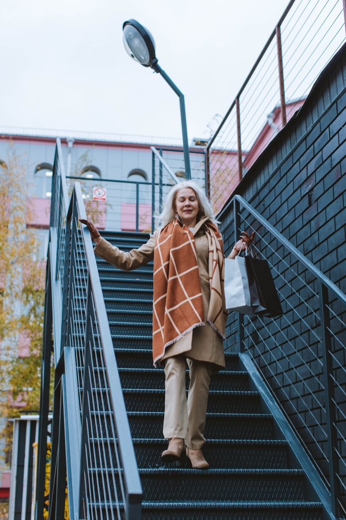 Elegant senior woman with shopping bags walking down outdoor staircase, embodying urban lifestyle.