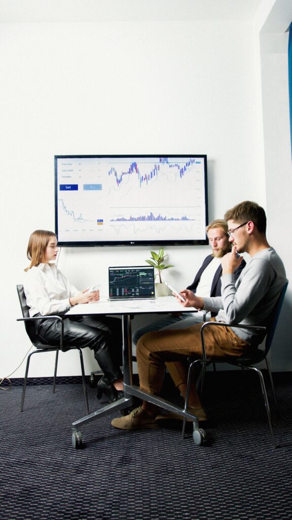pexels photo 5715850 5715850 Three business professionals in a meeting room discussing financial charts displayed on a screen.
