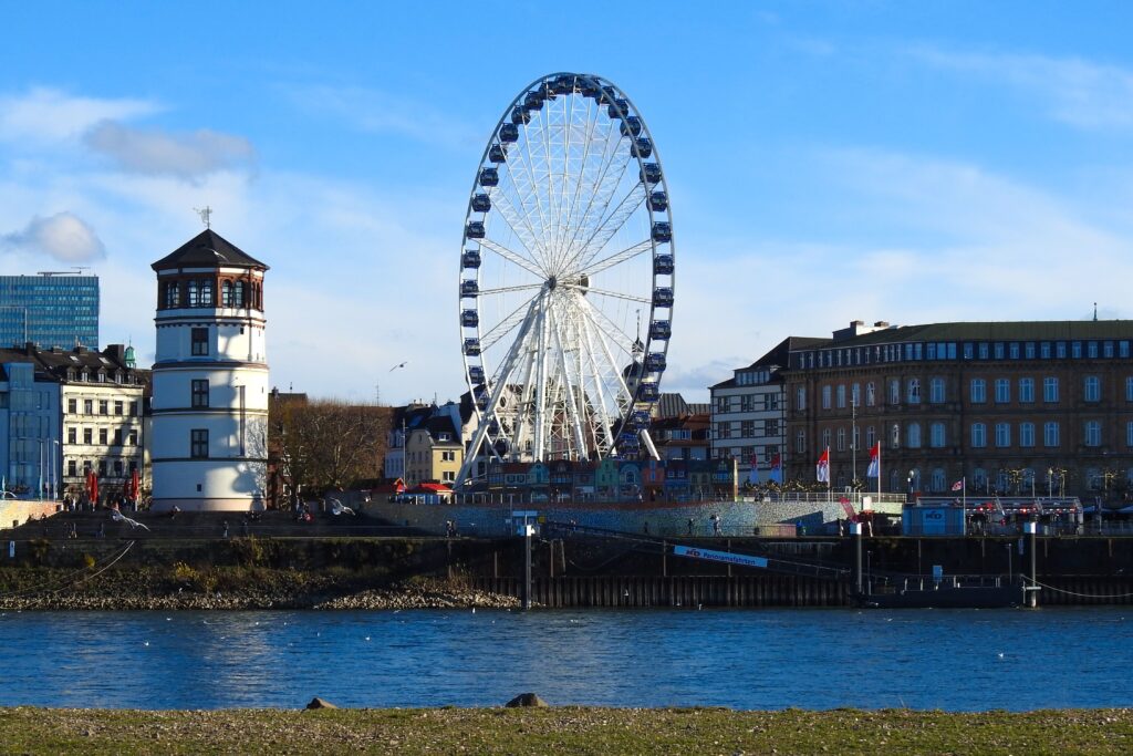 pexels photo 6106640 6106640 Panoramic view of a Ferris wheel by the river in Düsseldorf, Germany with clear blue skies.