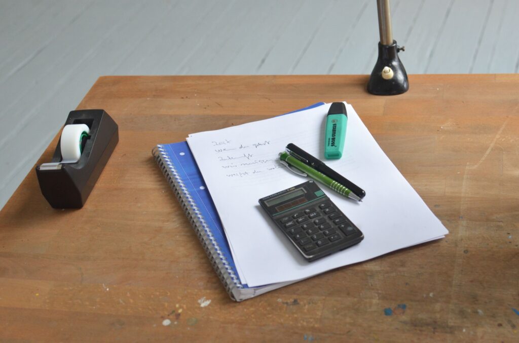 pexels photo 6368843 6368843 2 High angle of wooden desk with papers and small calculator with and pens on top near tape dispenser