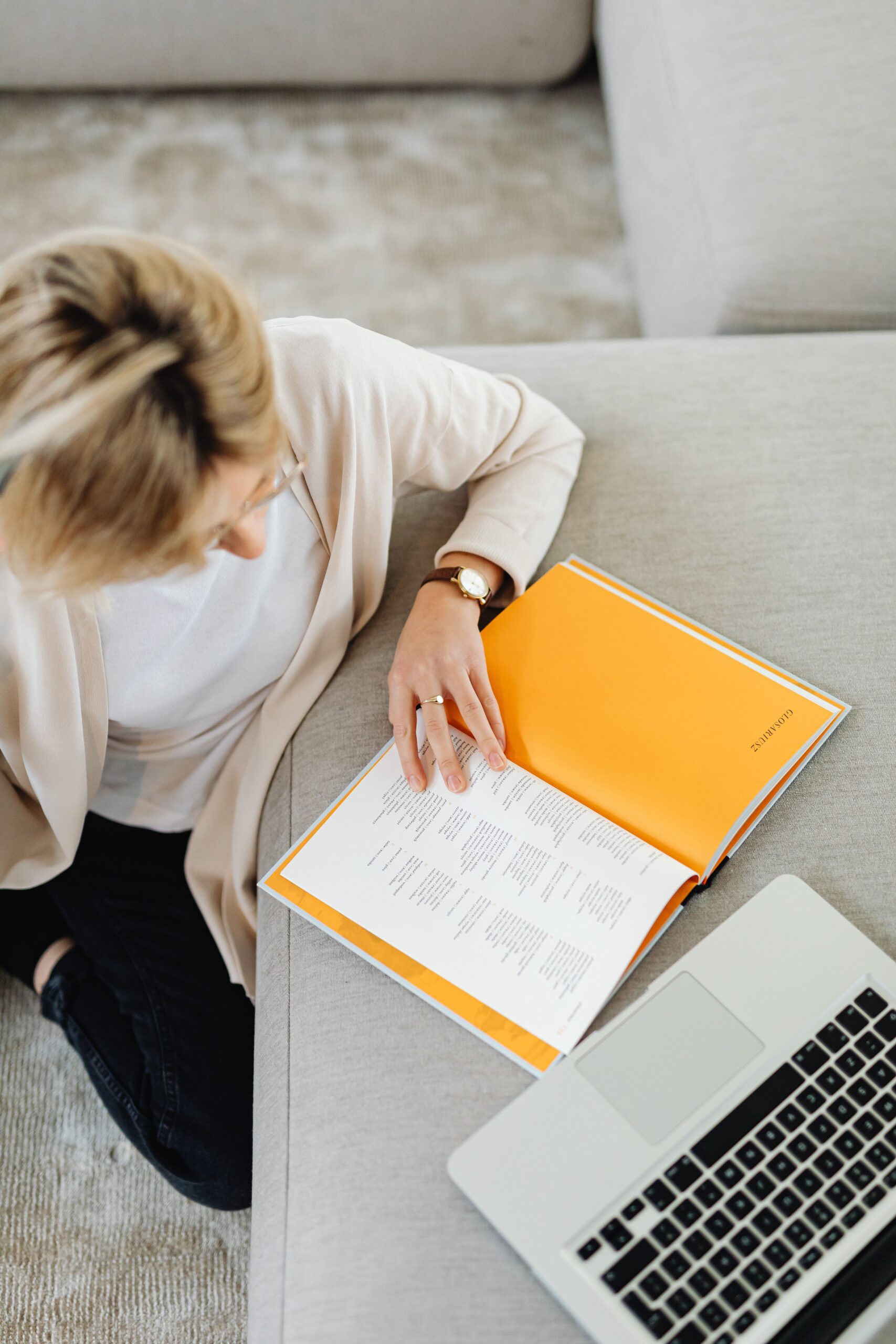 A woman reads a book in a cozy home setting with a laptop, creating a warm and focused environment.