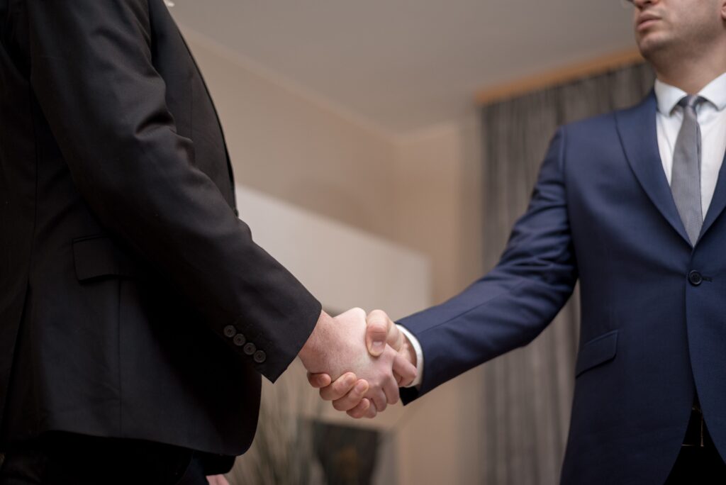pexels photo 6918507 6918507 Two businessmen in suits shaking hands, emphasizing trust and partnership indoors.