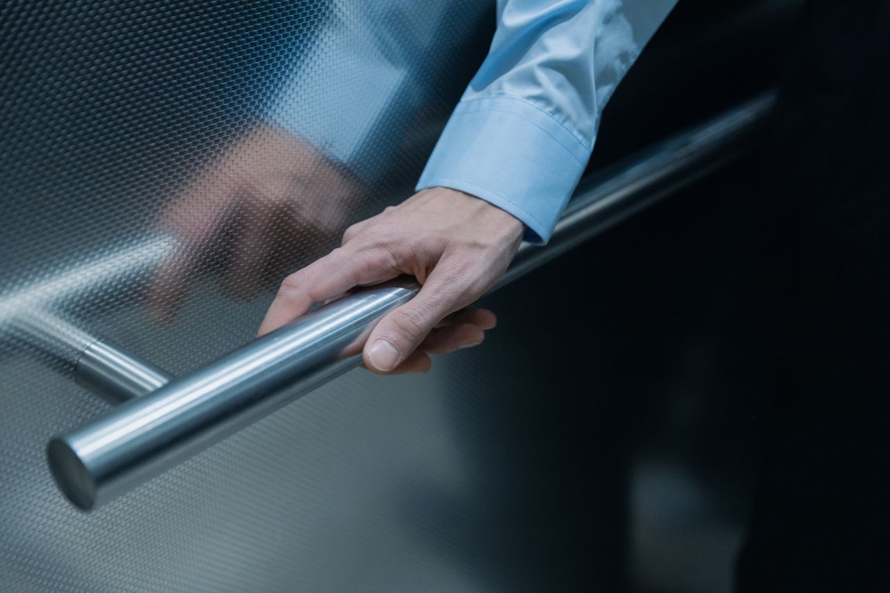 Treppenlift Kosten 2026: Preise, Zuschüsse und Spartipps im Überblick Close-up of a hand in a blue shirt holding onto a metal handrail in an elevator.
