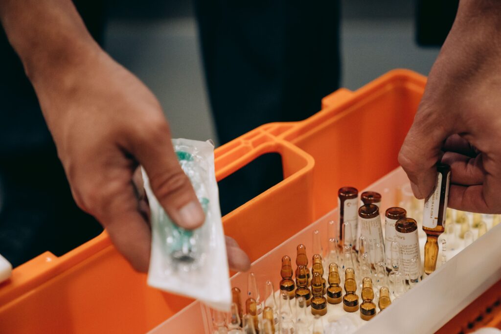 pexels photo 8943354 8943354 Close-up of hands organizing vials and syringe in a medical first aid kit, emphasizing emergency readiness.