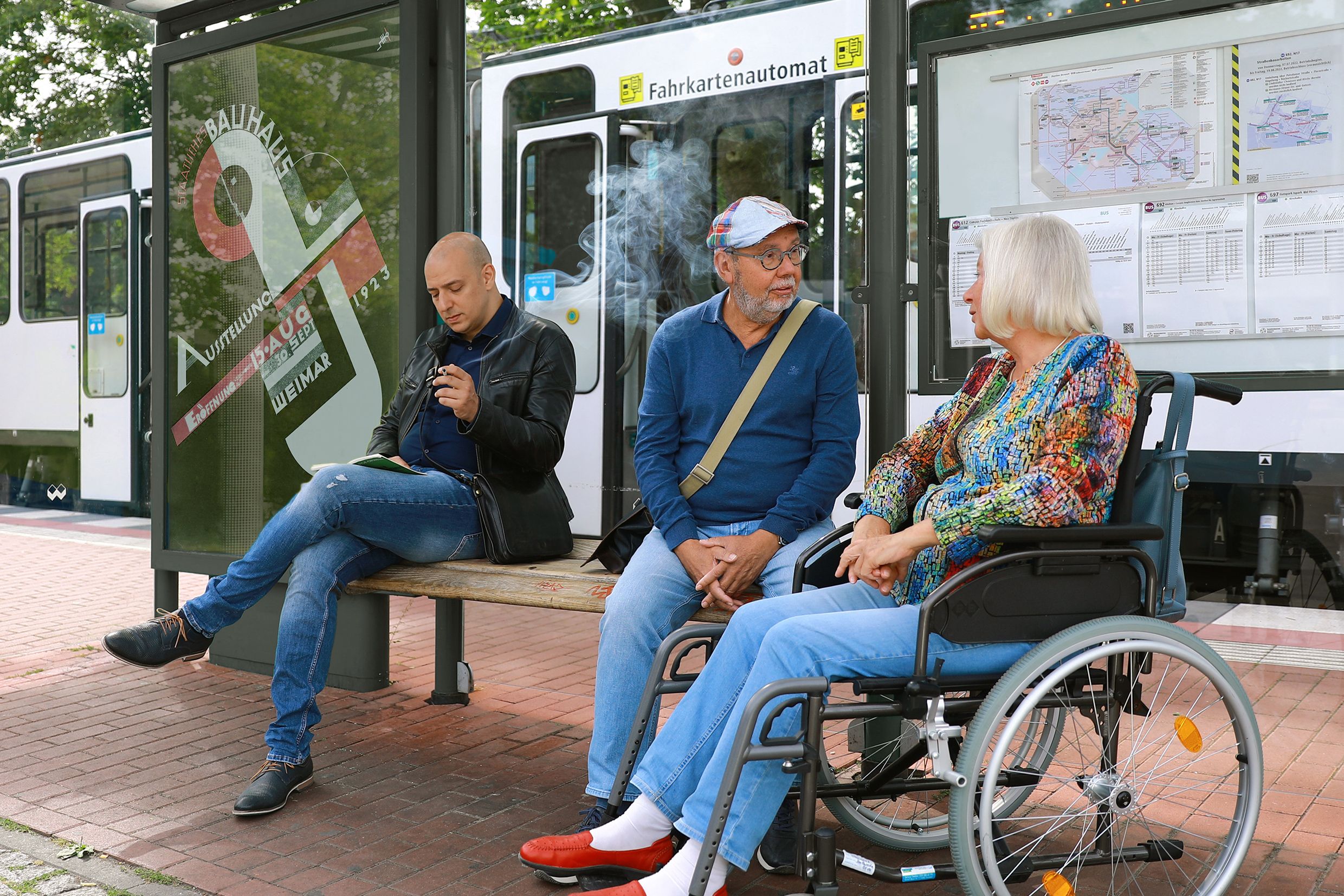 Treppenlift mit Akku Bochum – Vorteile bei Stromausfall Adults and a senior in a wheelchair waiting at a bus stop in Germany.