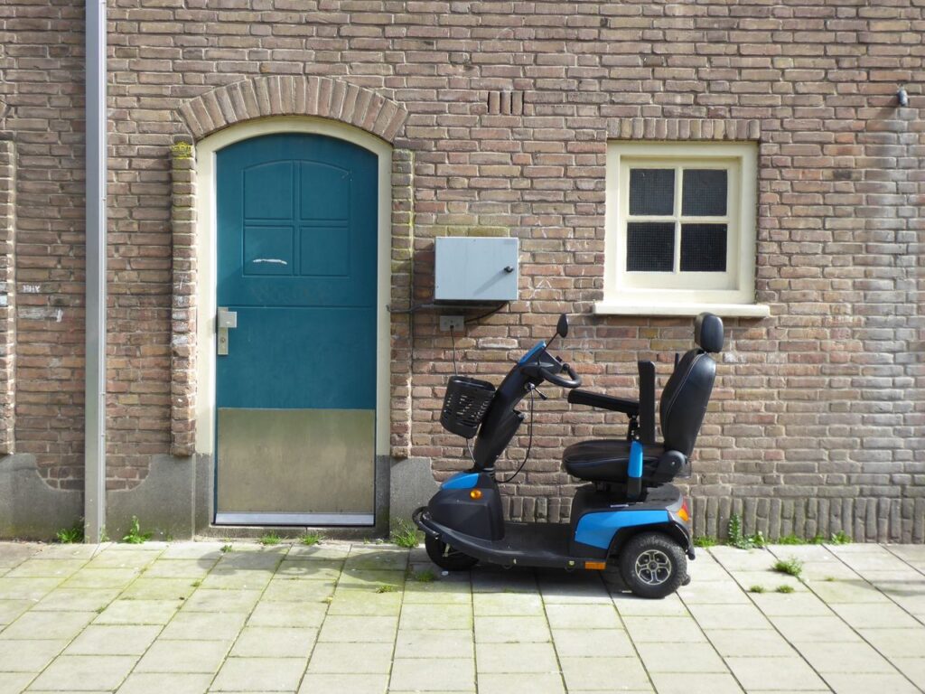 Treppenlift Pilot A blue mobility scooter parked beside a brick wall with a door in Amsterdam.