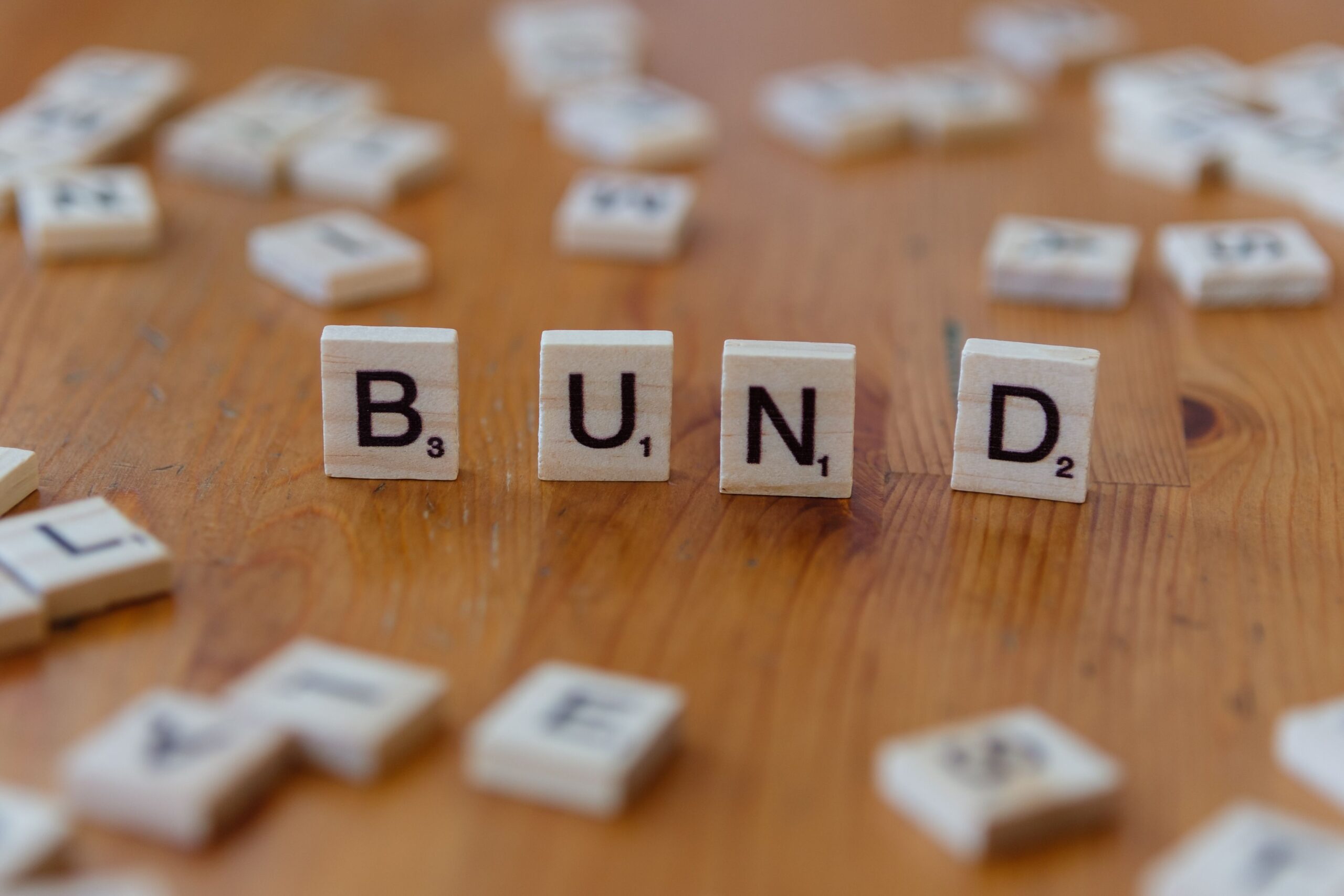 Close-up of Scrabble letters forming 'BUND' on a wooden surface, game concept.