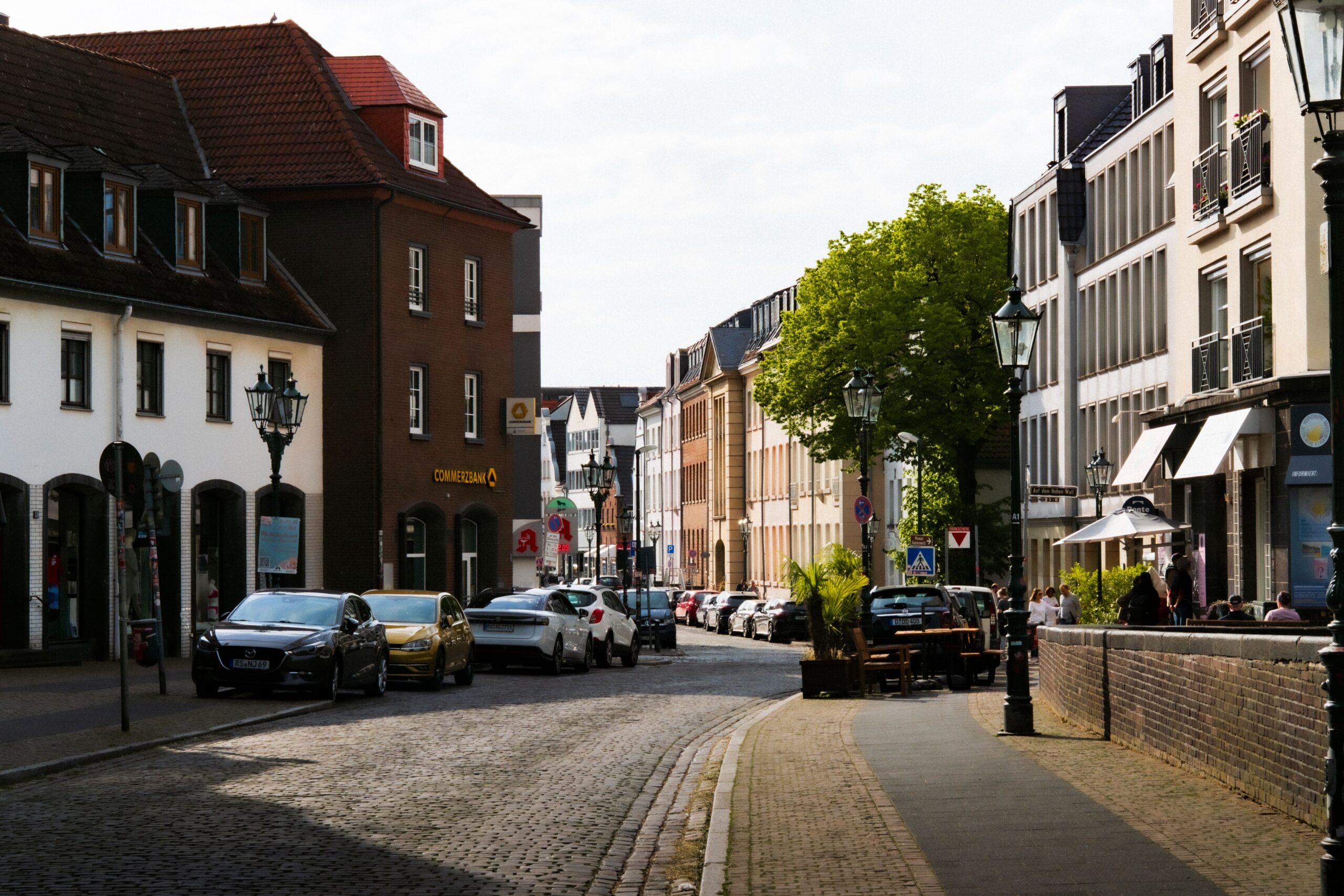 Hublift vs. Plattformlift Dortmund: Welcher ist der richtige für Sie? Sunny day on a cobblestone street in Düsseldorf, Germany with parked cars and classic architecture.