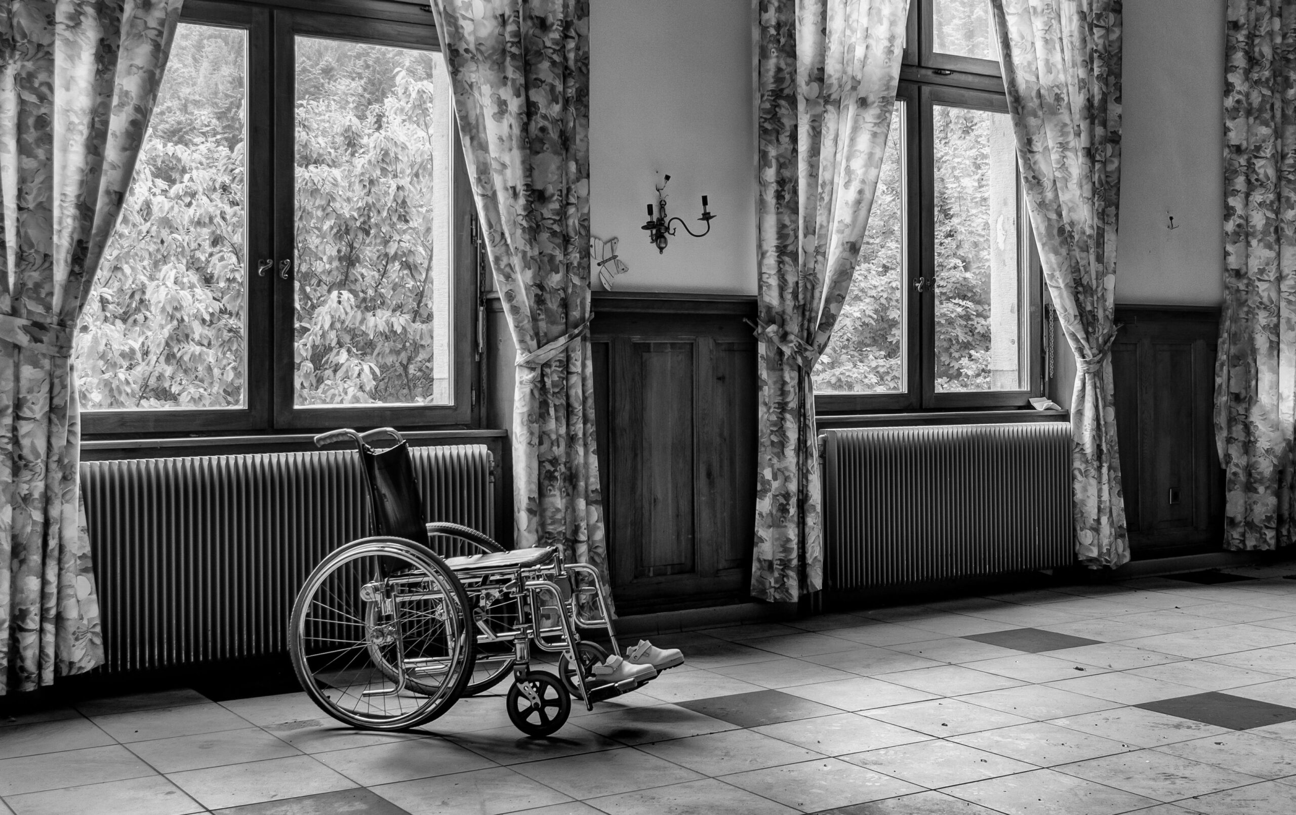 Treppenlift für pflegende Angehörige Gelsenkirchen – Entlastung im Alltag Black and white photo of an empty room with a wheelchair by large windows.